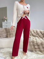 Woman showing the tie detail on the waistband of red ribbed pants, worn with a cream long-sleeve top.