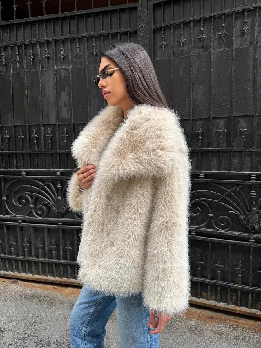 Woman wearing a cream-colored faux fur jacket with blue jeans and sunglasses, standing in front of a black metal gate. Main image