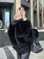 Back view of a woman wearing a black faux fur jacket and studded jeans, carrying a handbag