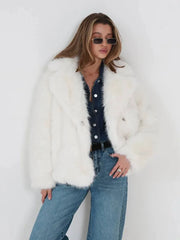 Front view of a woman in a white faux fur jacket, denim shirt, and blue jeans, with hands in pockets.