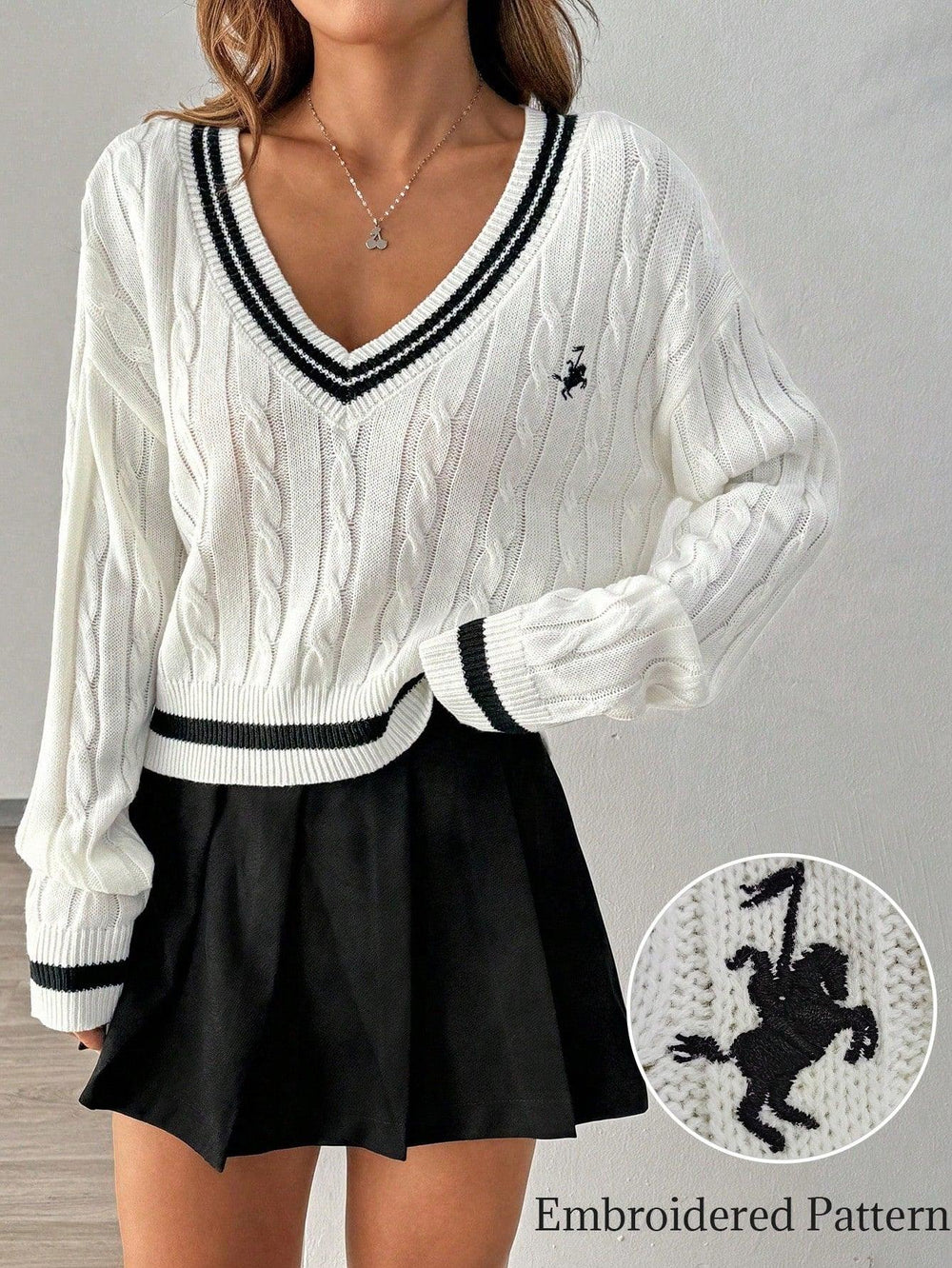 Close-up of the embroidered logo on the white cable knit sweater.