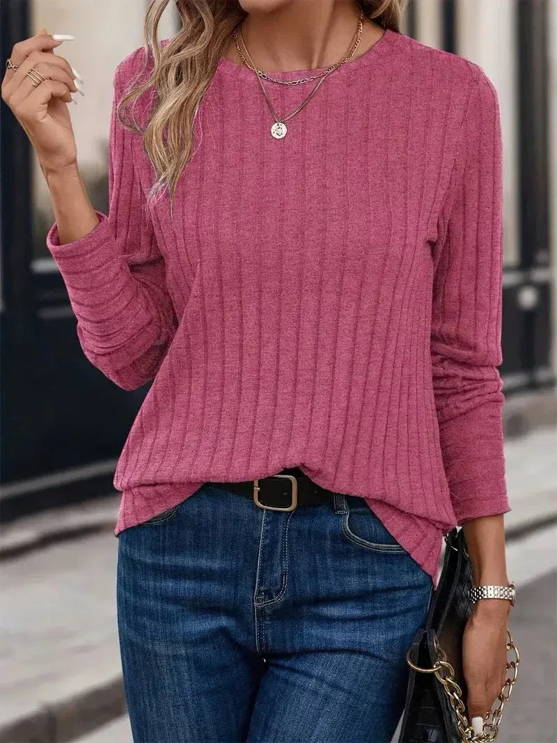 Woman wearing a pink ribbed long-sleeve crew neck top with dark wash jeans and a black belt