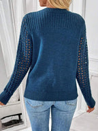 Back view of a woman wearing a blue knit sweater with cutout sleeves and blue jeans.