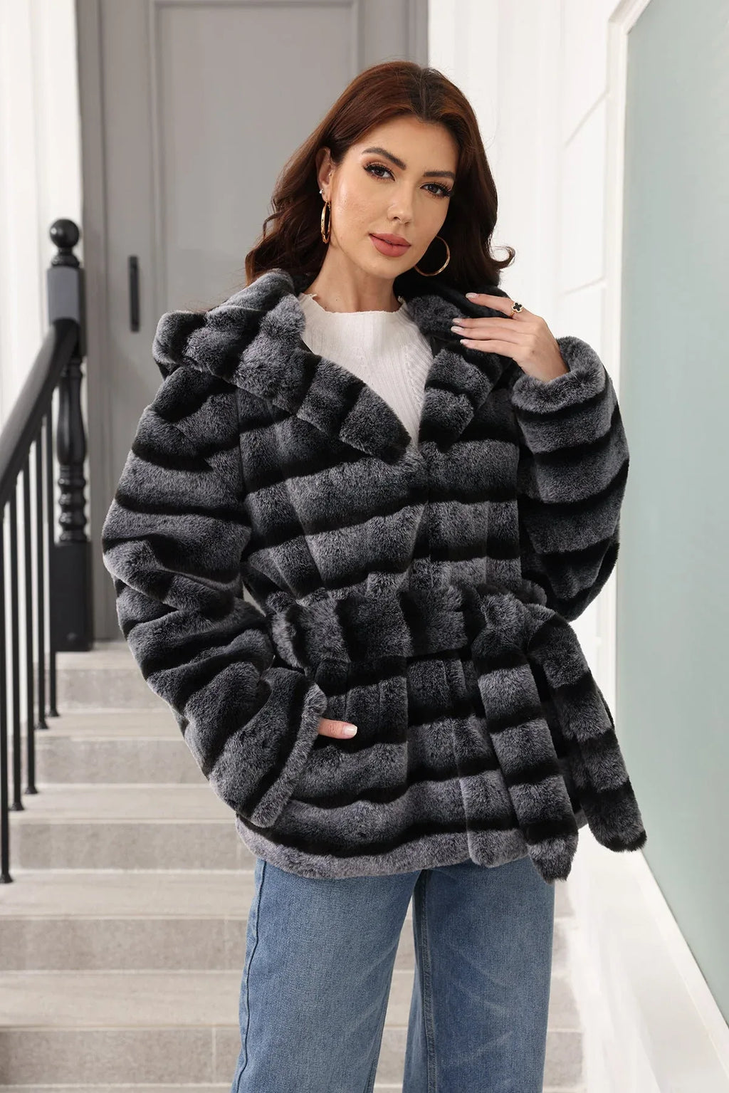 Woman posing in a hooded faux fur jacket with horizontal stripes and a belted waist.