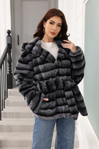 Woman posing in a hooded faux fur jacket with horizontal stripes and a belted waist.
