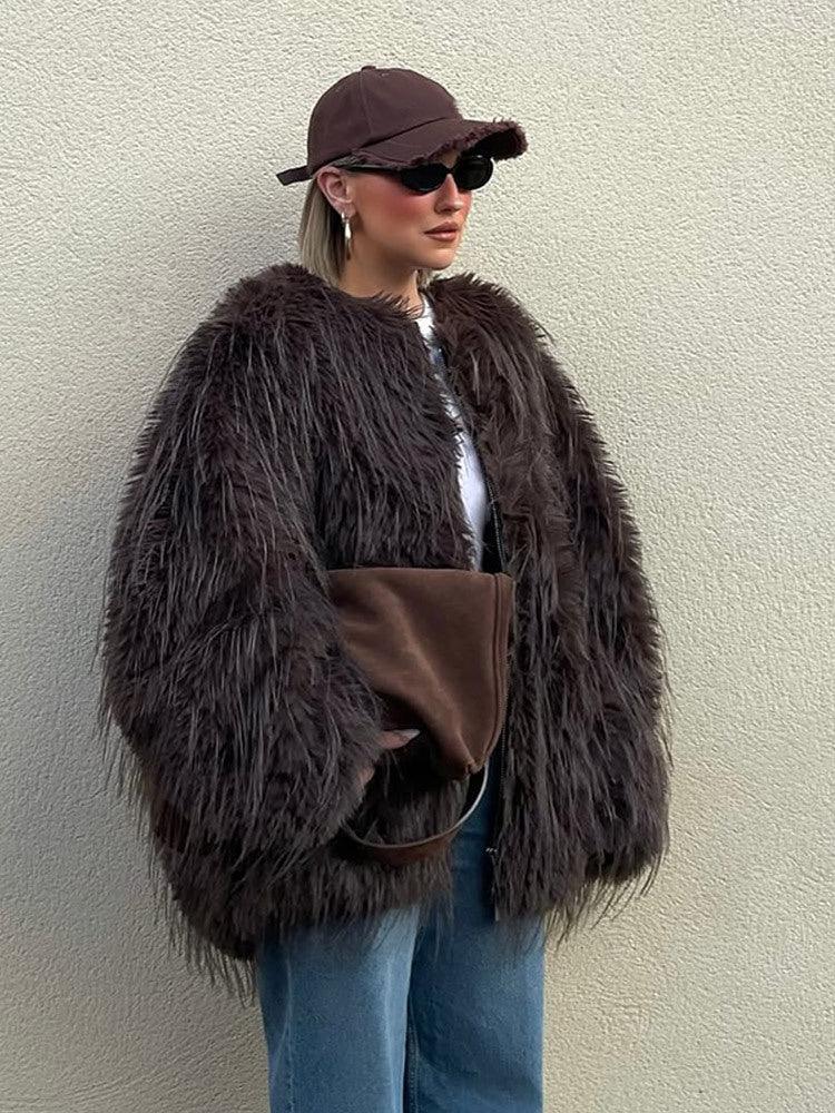 Woman wearing a brown shaggy faux fur jacket, blue wide-leg jeans, and a brown baseball cap.