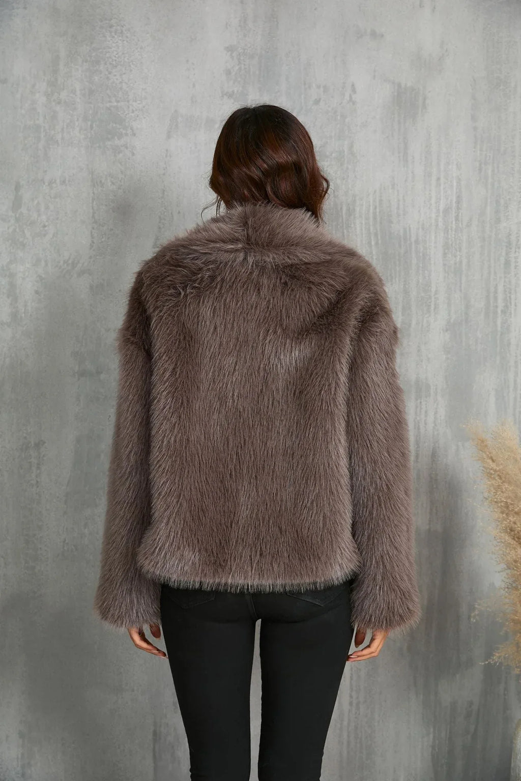 Back view of a woman wearing a brown faux fur jacket and black pants.