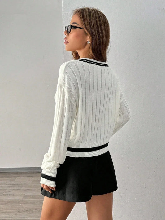 Woman wearing a white cable knit cropped sweater with black trim and a black pleated skirt, back view.