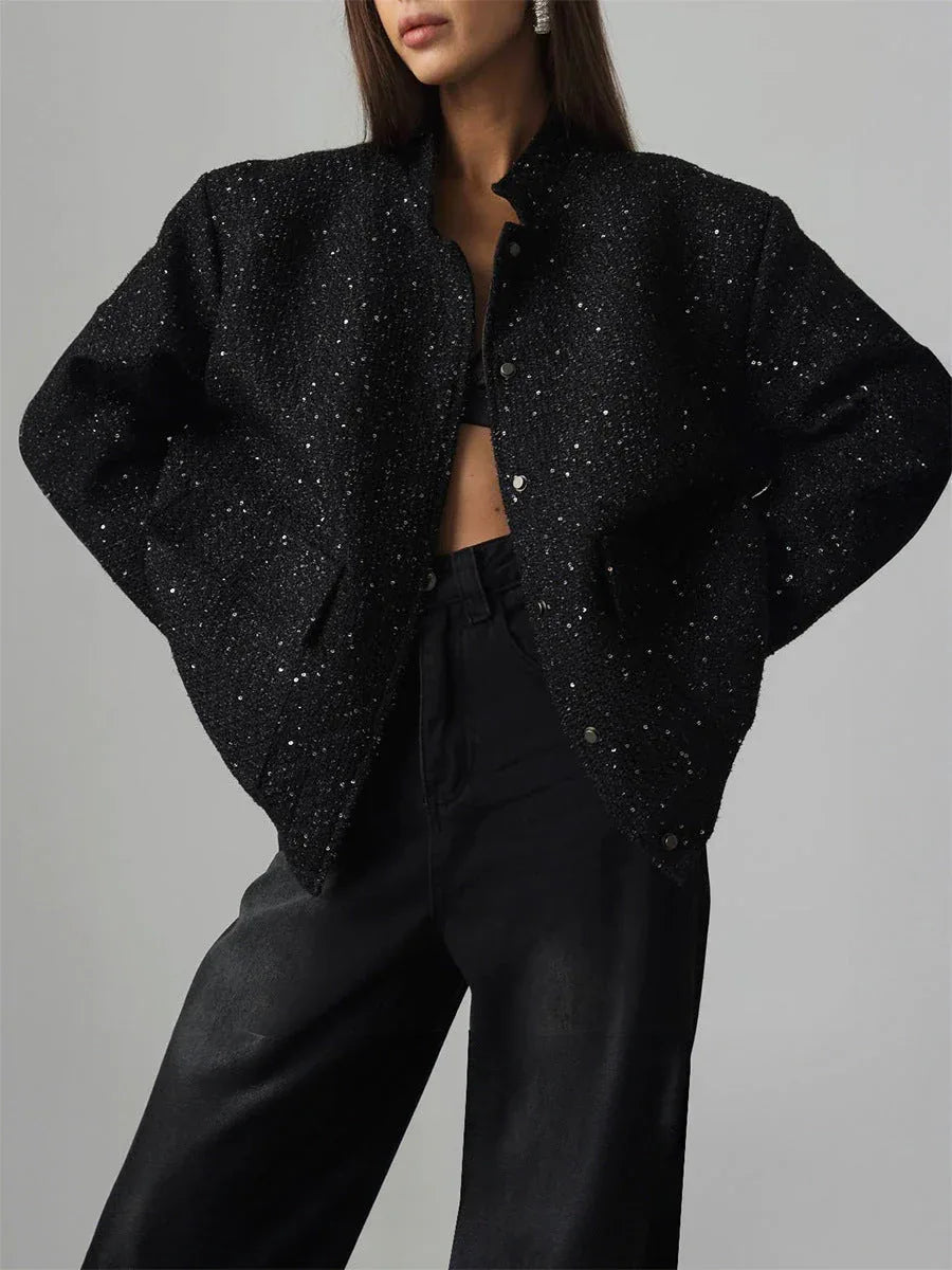 Woman wearing a black sparkly tweed cropped jacket over a black bra and black wide-leg jeans, hands on hips. Main image