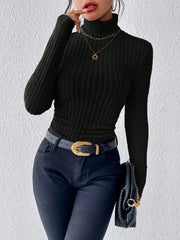 Woman wearing a black ribbed turtleneck sweater, black jeans, a black belt with a gold buckle, and holding a black clutch with a gold chain.