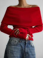 Close-up of a woman's hands wearing silver rings, wearing a red off-the-shoulder sweater with blue jeans.