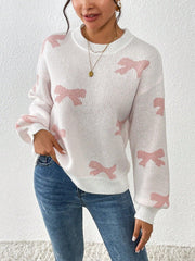 Close-up of a woman wearing a white crew neck sweater with pink bow print and blue jeans, showing the print detail