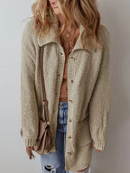 Woman wearing a long beige knit cardigan over a brown henley top and blue jeans