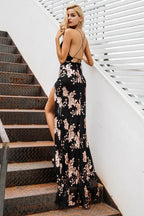 Back view of a woman in a black sequined floral print evening gown with a high leg slit and cross back straps