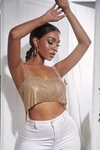 Woman with arms raised, wearing a gold rhinestone crop top and white pants