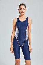 Woman in a navy blue one-piece swimsuit with geometric side panels, standing and facing forward