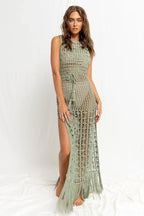 Woman wearing a green crochet knit maxi dress with a high slit and fringe hem, front view.