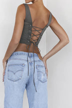 Back view of a woman wearing a khaki ruched corset top with a lace-up back detail and denim jeans.