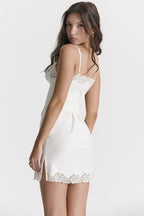 Back view of a woman in a white slip dress with lace trim and side slit.