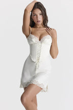 Woman in a white slip dress with lace trim and corset detail, posing with arm raised.