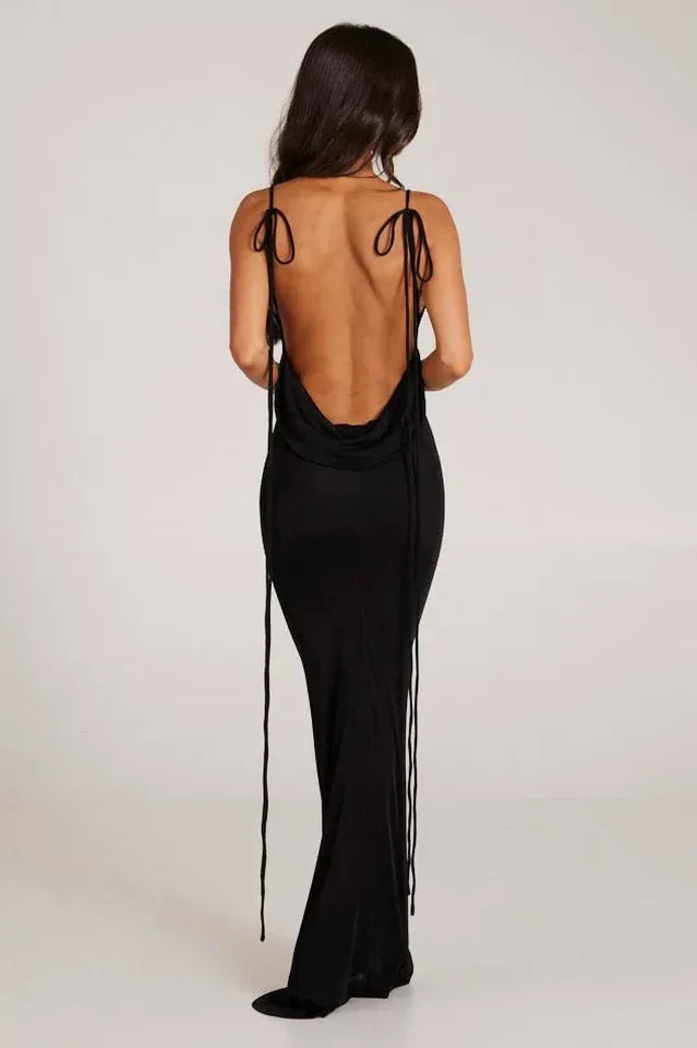 Woman wearing a long black sleeveless cowl neck dress with an open back and adjustable spaghetti straps.