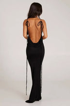 Woman wearing a long black sleeveless cowl neck dress with an open back and adjustable spaghetti straps.
