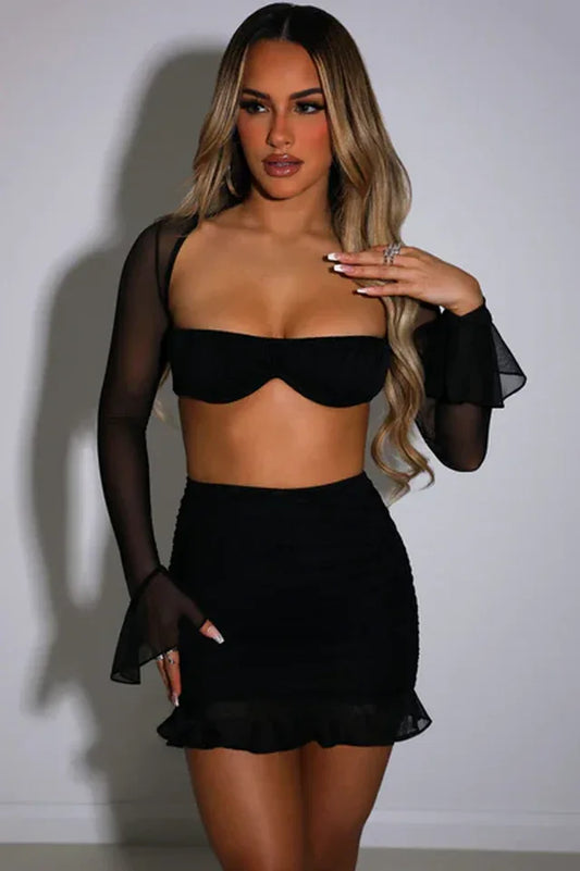 Woman wearing a black mesh two-piece set with a square neck bra top and ruched mini skirt with ruffle hem.