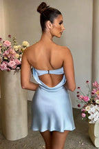 Back view of a woman in a light blue strapless satin slip dress showing the open back and bow detail