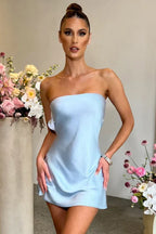 Woman wearing a light blue strapless satin slip dress with an open back and bow detail