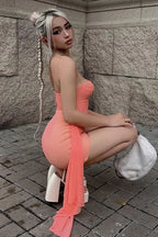 Model in a coral ruched mini dress, showcasing the fit and detailing, while kneeling outdoors.
