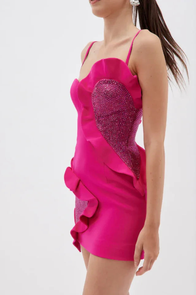 Side profile of a model in a flamboyant pink mini dress featuring ruffled layers and sparkling embellishments.