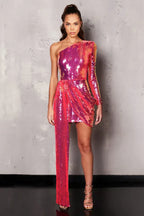 Woman wearing a pink and purple sequined one-shoulder mini dress with an asymmetrical hemline and a long draping detail, standing against a grey textured wall.