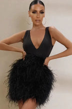 Woman in a black feather mini dress with a deep V-neckline and hands on hips.