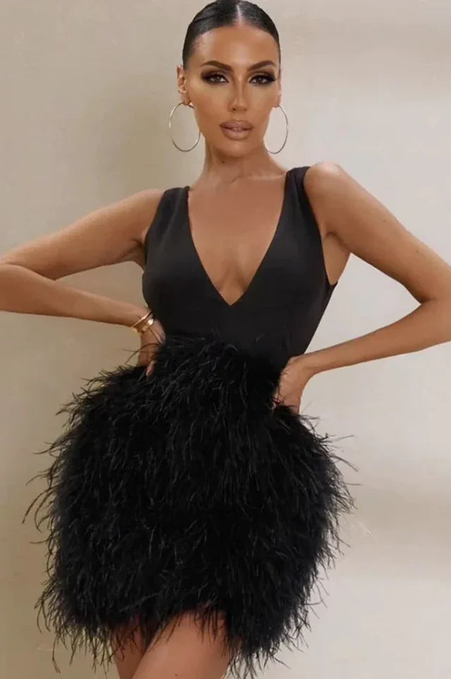 Woman in a black feather mini dress with a deep V-neckline and hands on hips.