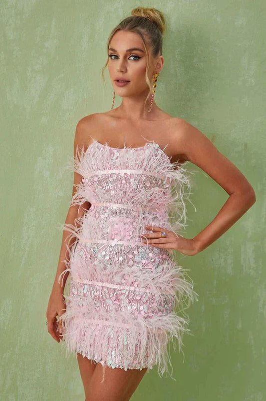 Woman wearing a pink strapless sequin mini dress with feather trim and statement earrings, posing with one hand on her hip.