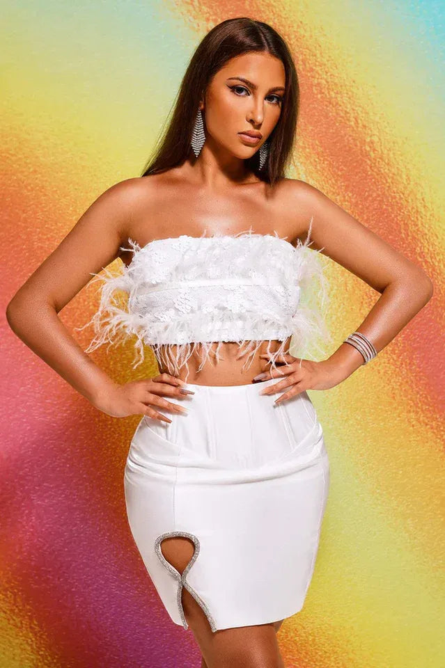 Woman wearing a white strapless feather and sequin crop top with a white high-waisted satin skirt with a cut-out detail. Main image