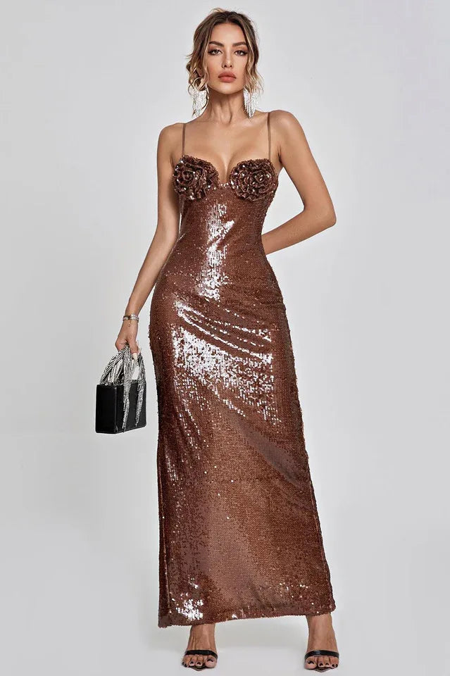 Woman in a shimmering bronze sequined evening gown with floral applique bust detail, spaghetti straps, and a floor-length hem.