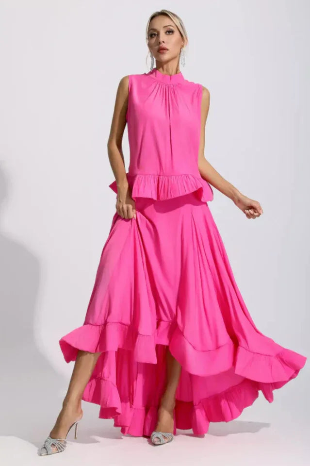 Woman wearing a bright pink sleeveless mock neck top with a ruffled peplum and a high-low maxi skirt with tiered ruffles. Main image