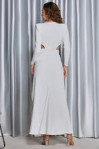 Back view of a woman in a white formal dress, showcasing the back cut-outs and flowing skirt.