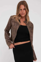 Woman wearing a brown faux leather cropped jacket with a black tank top and black skirt, front view.