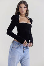 Side view of a model in a black velvet long-sleeve top with a square neckline and puffed shoulders, paired with light-wash denim jeans.