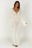 Woman wearing a long white crochet knit dress with bell sleeves and a deep V-neckline, front view