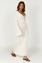 Woman wearing a long white crochet knit dress with bell sleeves and a deep V-neckline, side view