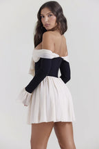 Rear view of a woman in a black and ivory off-the-shoulder mini dress with a bow and flared sleeves.