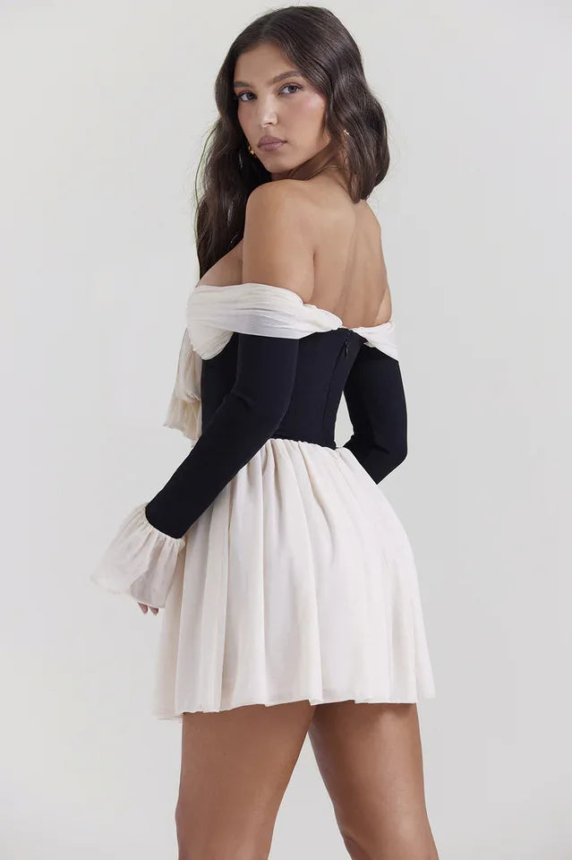 Rear view of a woman in a black and ivory off-the-shoulder mini dress with a bow and flared sleeves.