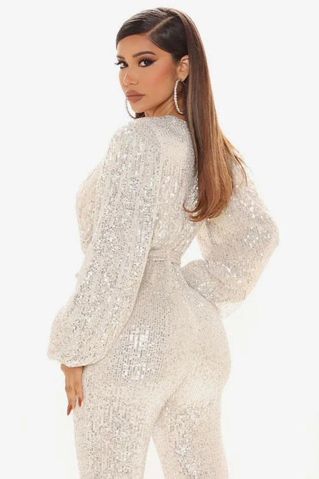 Close-up back view of a woman in a white sequined jumpsuit with a V-neck and balloon sleeves