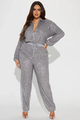 Woman wearing a grey sequined long-sleeved collared jumpsuit with a zipper front closure and drawstring waist. The pants have a grey side stripe.