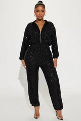 Woman wearing a black sequined long-sleeved collared jumpsuit with a zipper front closure and drawstring waist.
