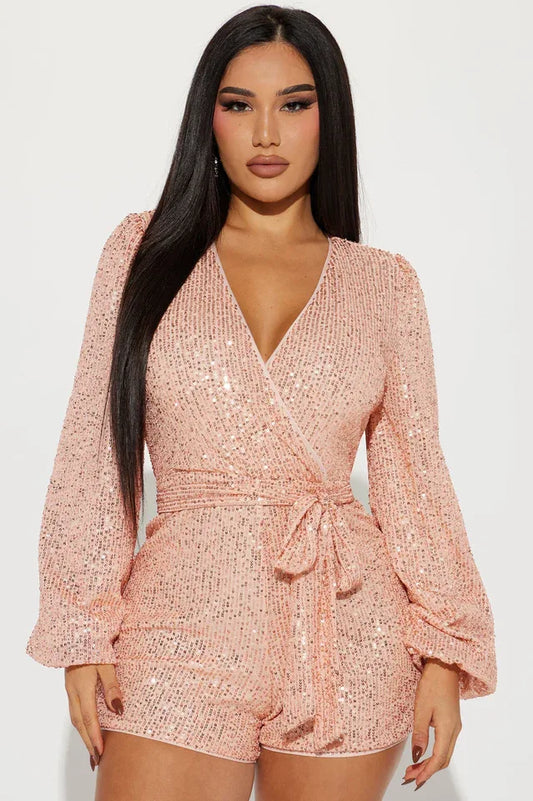 woman wearing a pink sequin romper with long puffed sleeves and a tie waist
