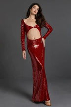Woman with long dark hair wearing a long red sequin dress with cut-out details and long sleeves, standing against a grey background
